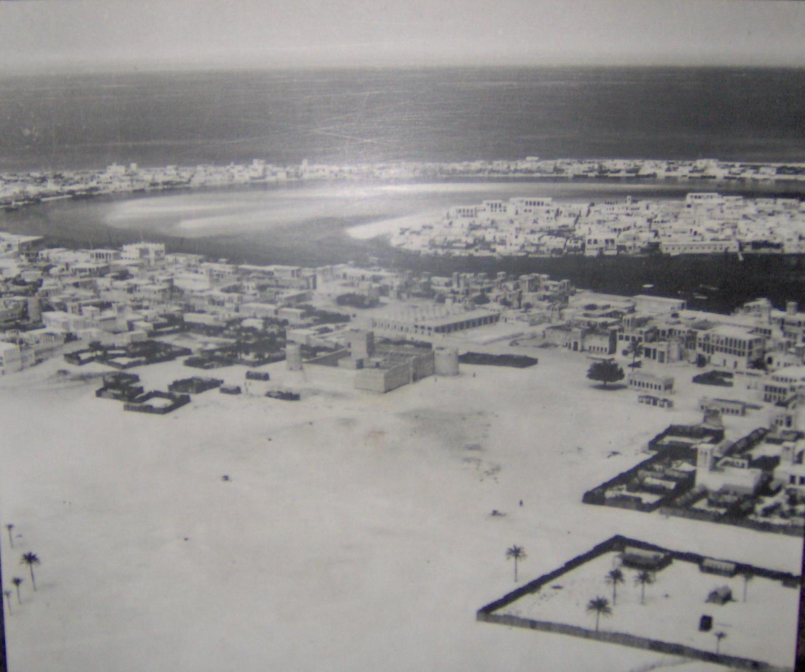 Dubai pada tahun 1950: area dalam foto ini menunjukkan Bur Dubai di latar depan (berpusat di Benteng Al-Fahidi), Deira di tengah-kanan di sisi lain sungai, dan Al Shindagha (kiri) serta Al Ras (kanan) di latar belakang di seberang sungai, dari Deira.