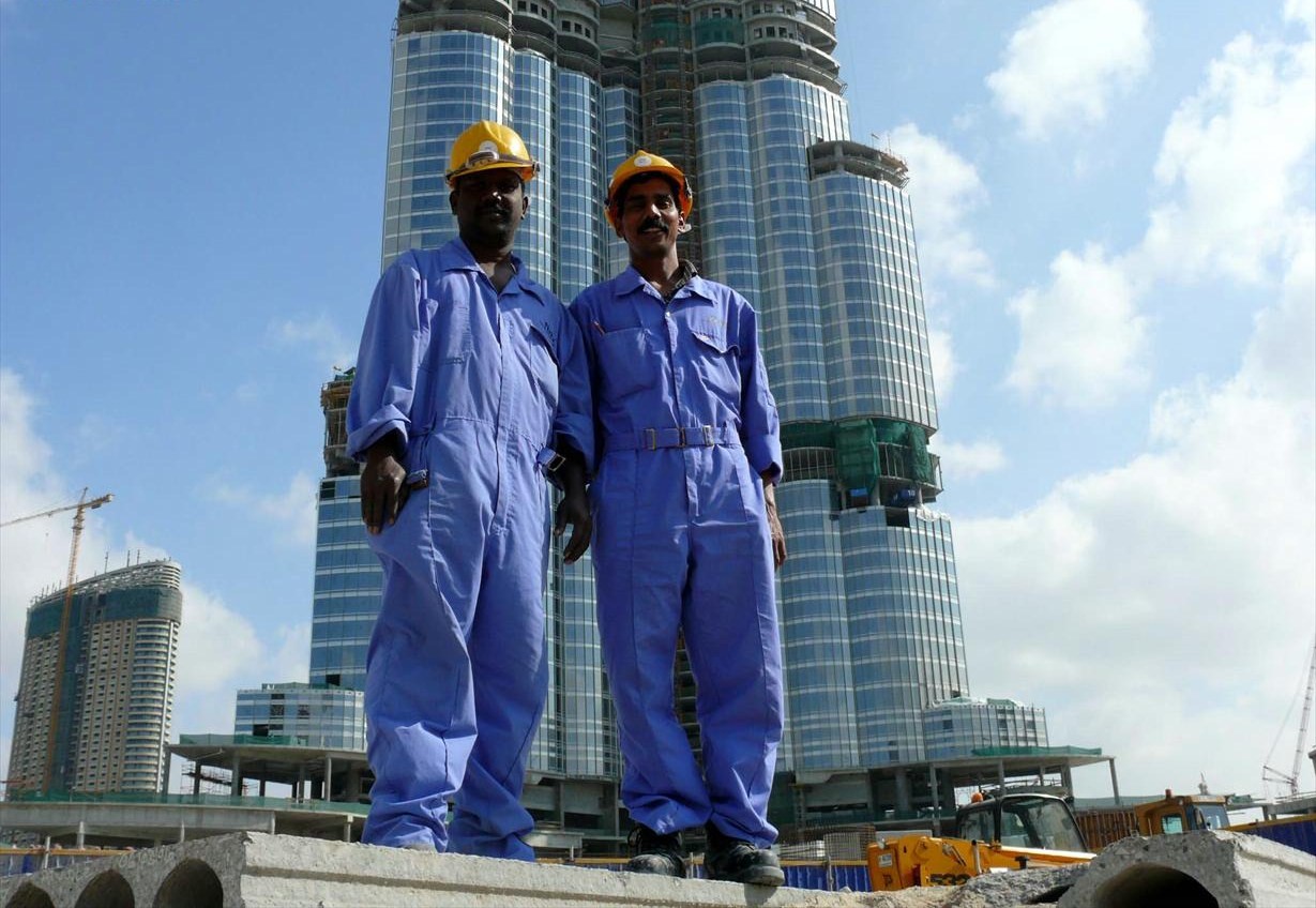 Dua pekerja kerah biru Asia Selatan berpose untuk foto dengan Burj Khalifa di latar belakang