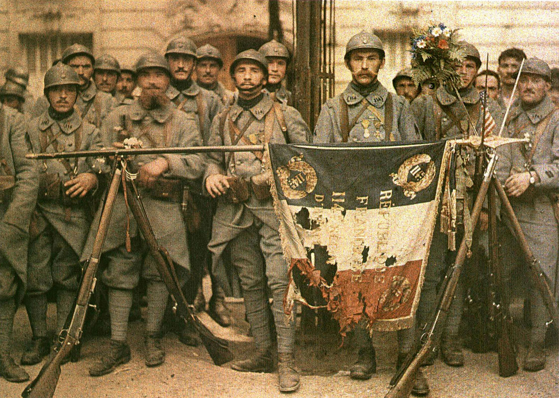 Para Poilu Prancis berpose dengan bendera mereka yang terkoyak perang pada tahun 1917, selama Perang Dunia I, sebuah konflik yang menelan korban jiwa sangat besar dan berdampak mendalam pada masyarakat Prancis.