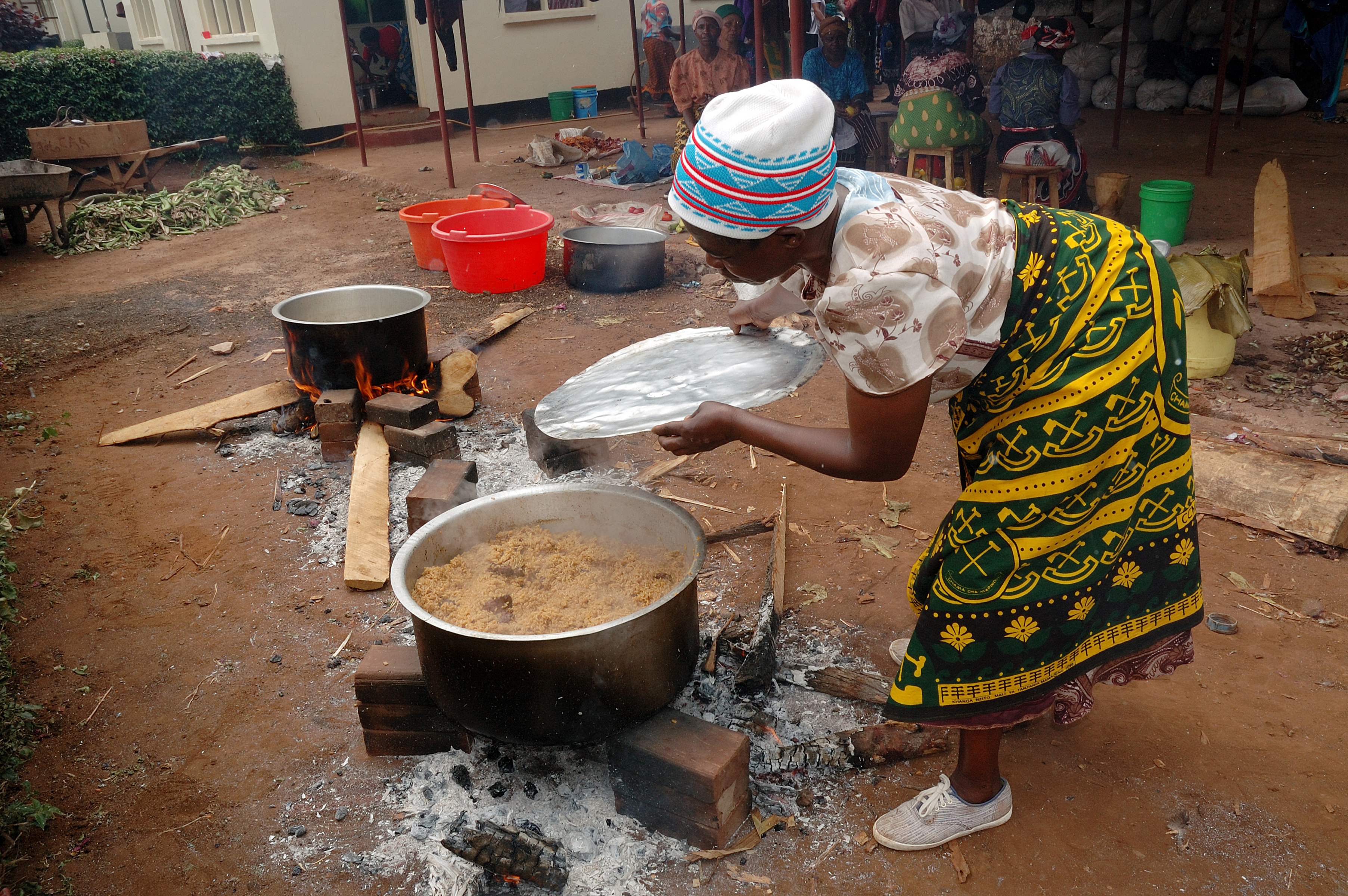 Seorang wanita Tanzania memasak hidangan nasi Pilau mengenakan Kanga tradisional.