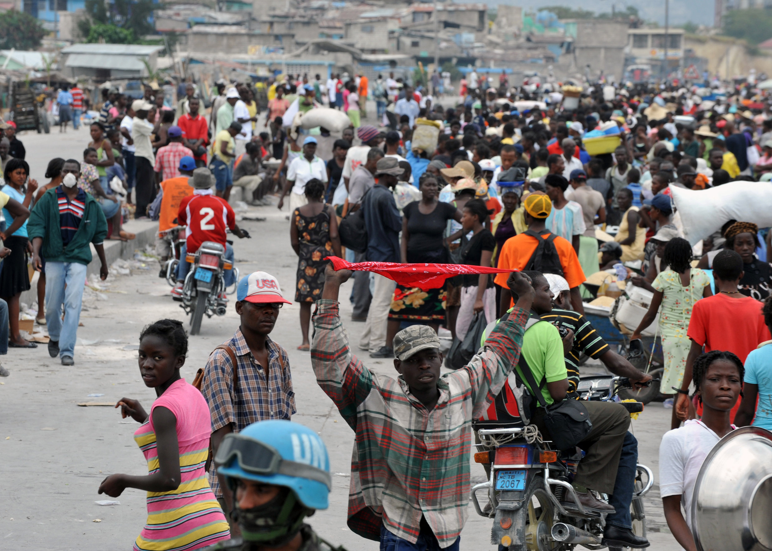 A street scene in Port-au-Prince, showing Haitian citizens and a UN Peacekeeper. The population is predominantly of African descent.
