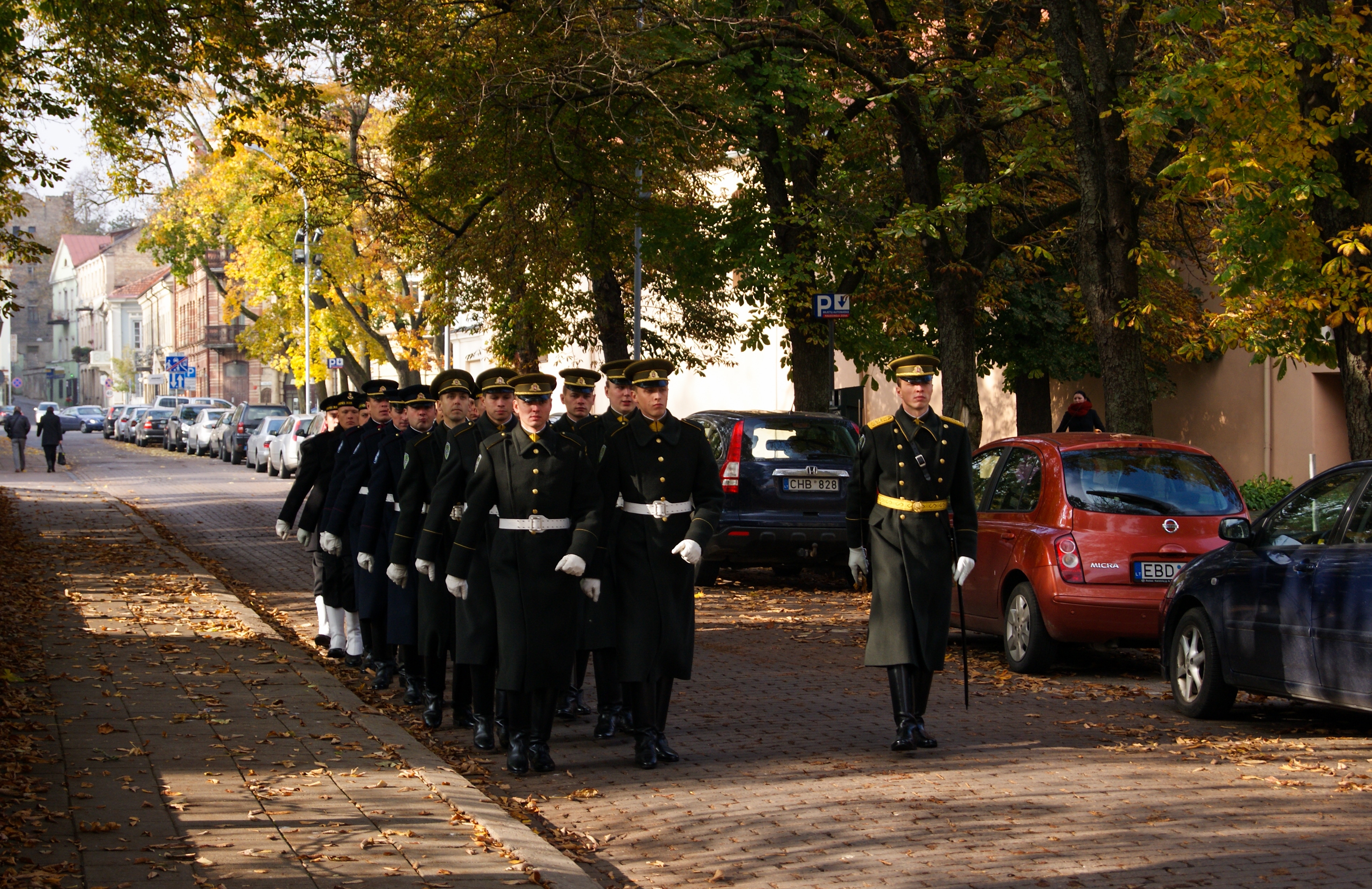 Lithuanian Army soldiers marching in dress uniforms in Vilnius. An officer with a sword leads the formation.