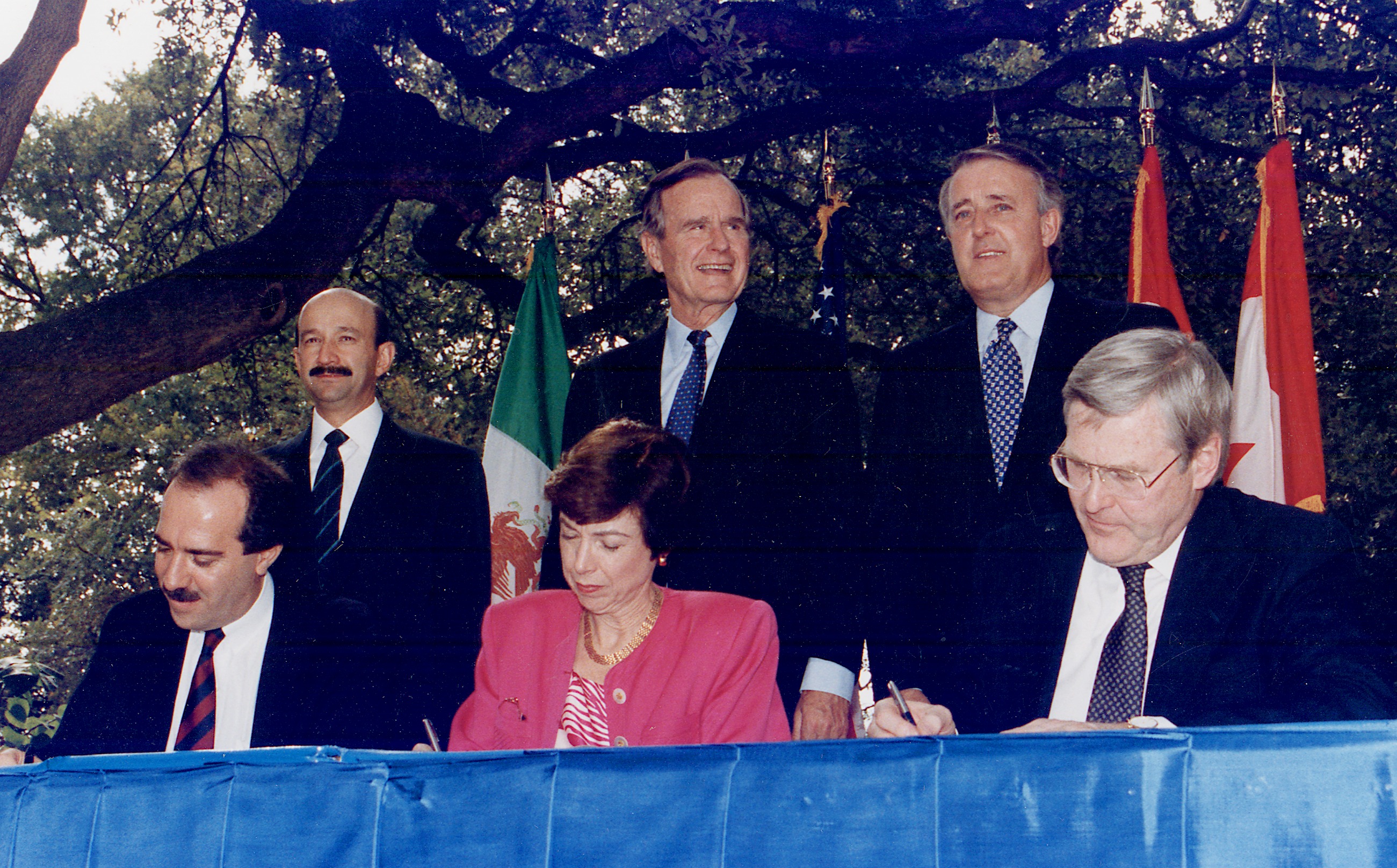 Lễ ký kết NAFTA, tháng 10 năm 1992. Từ trái sang phải: (đứng) Tổng thống Carlos Salinas de Gortari (México), Tổng thống George H. W. Bush (Hoa Kỳ), và Thủ tướng Brian Mulroney (Canada).