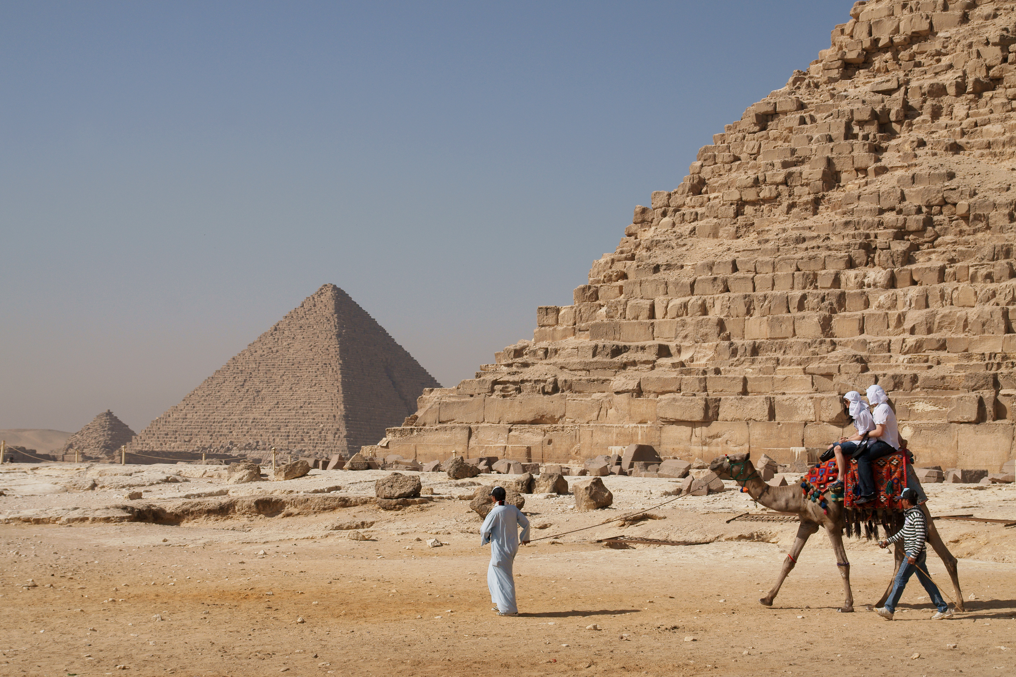 Tourists riding an Arabian camel in front of Pyramid of Khafre. The Giza Necropolis is one of Egypt's main tourist attractions, contributing significantly to the economy but also facing challenges of sustainability and equitable benefit distribution.