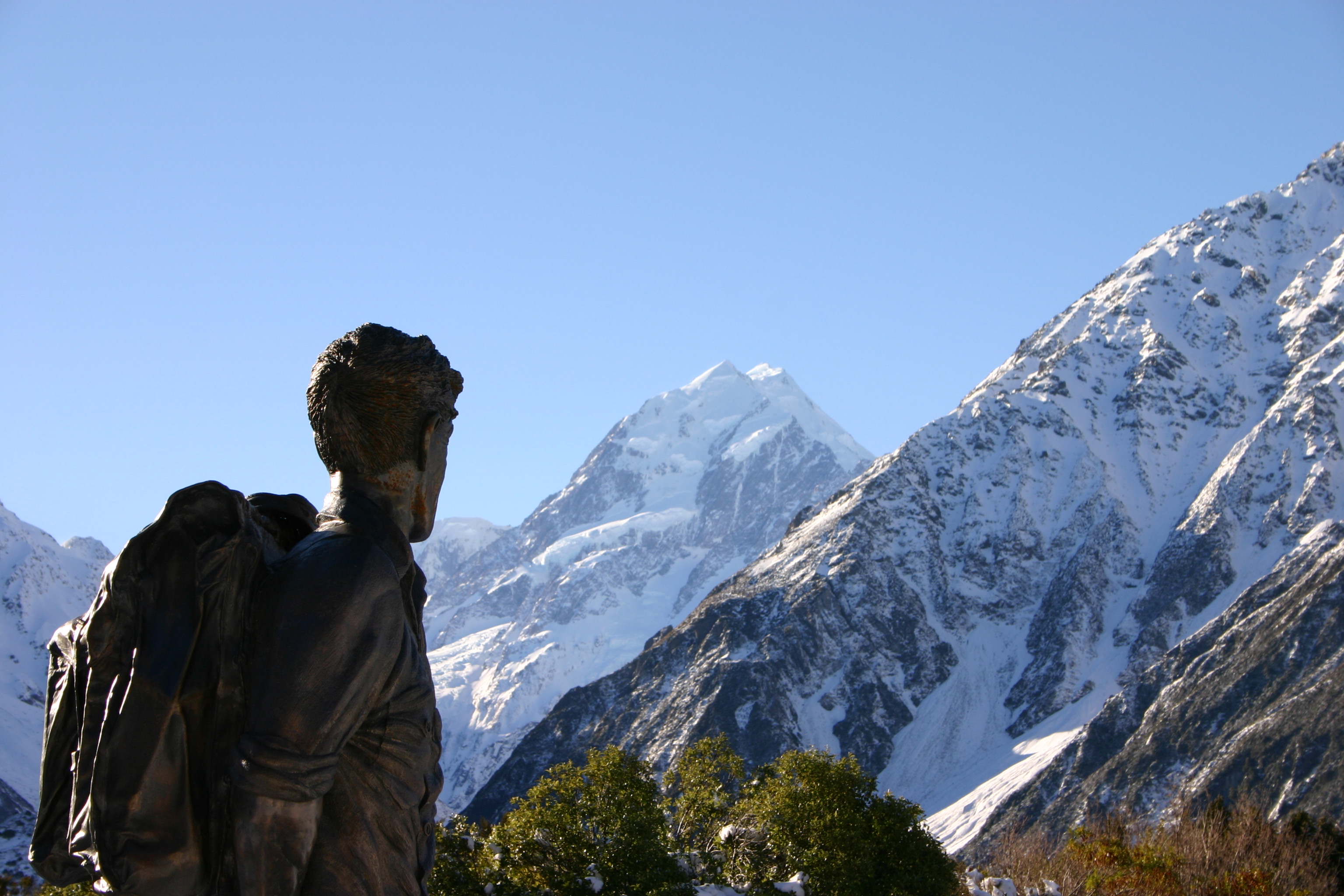 alt=雪を頂いた山を背景にした男性の像。
