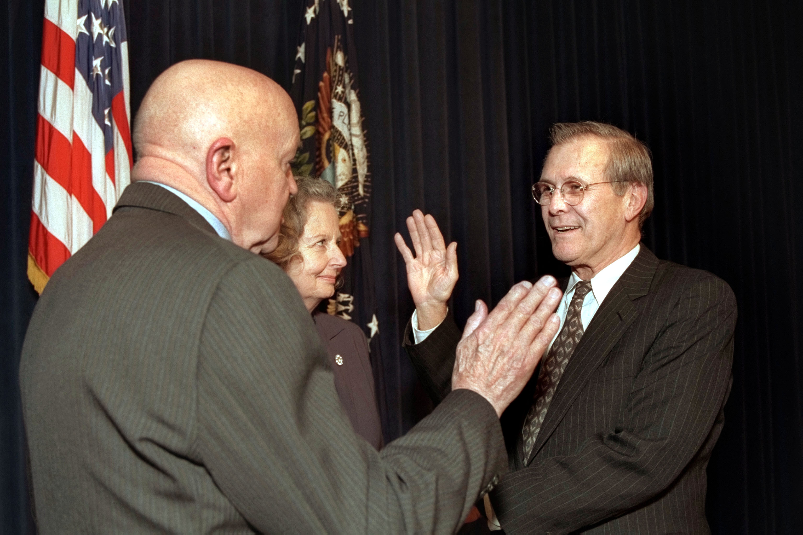 Rumsfeld mengangkat sumpah sebagai Setiausaha Pertahanan ke-21 pada 20 Januari 2001, oleh Pengarah Pentadbiran dan Pengurusan (Jabatan Pertahanan) David O. Cooke (kiri), sambil Joyce Rumsfeld memegang Alkitab dalam satu majlis di Bangunan Pejabat Eksekutif Eisenhower.