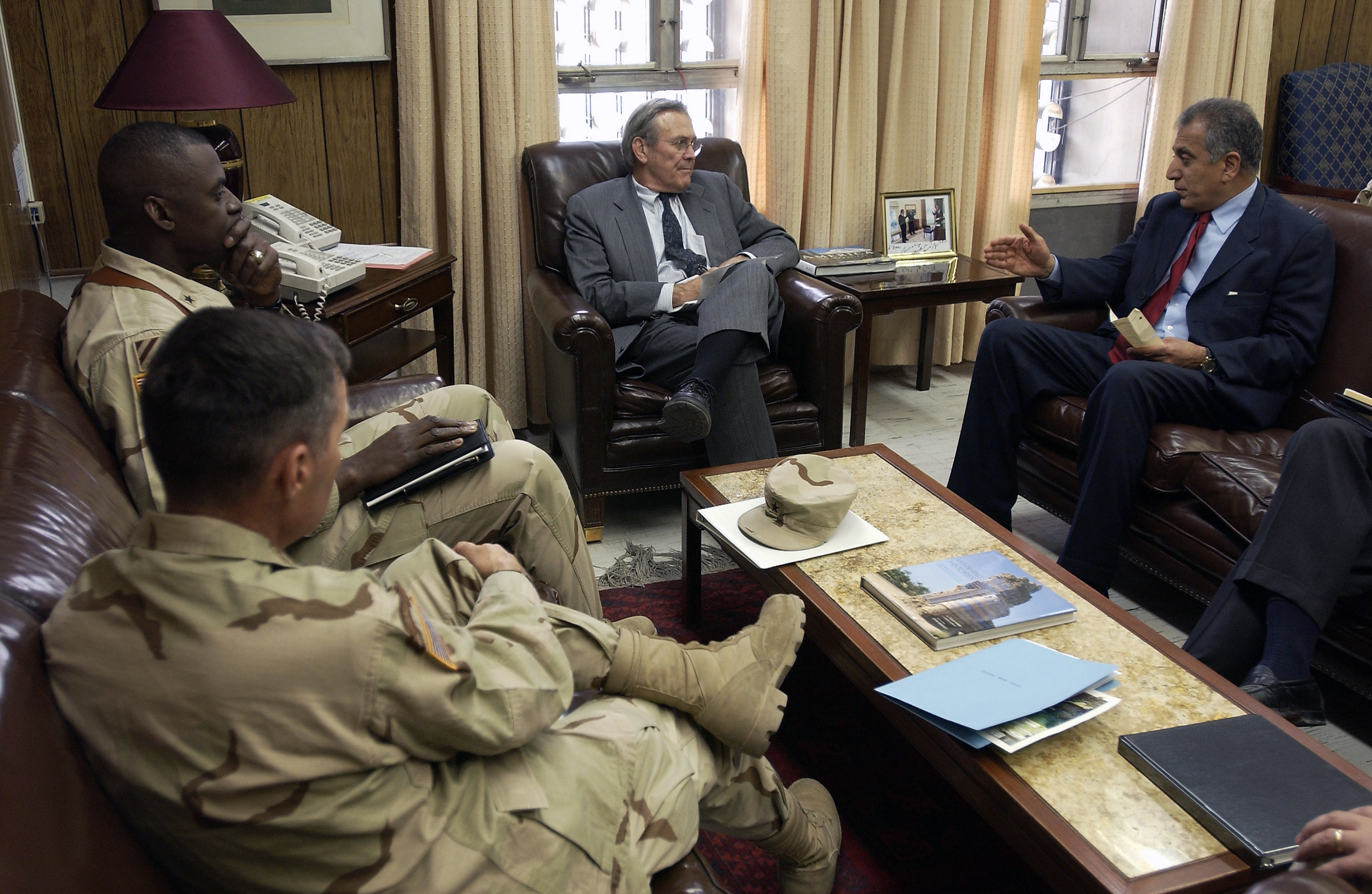 Rumsfeld (tengah) berbual dengan Duta Besar A.S. ke Afghanistan Zalmay Khalilzad (kanan) sambil Brig. Jen. Lloyd Austin (atas kiri) memerhati semasa lawatan ke Kandahar, Afghanistan, pada 26 Februari 2004.