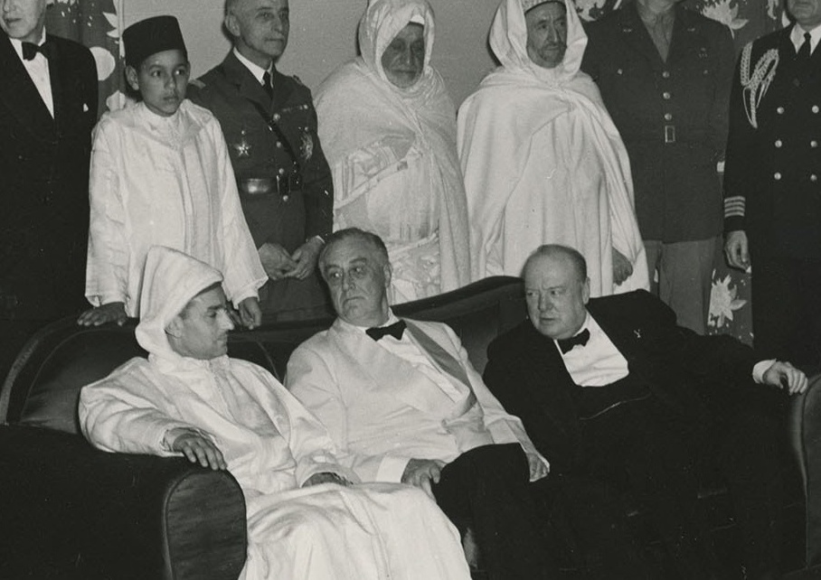 Sultan Mohammed seated with Franklin D. Roosevelt and Winston Churchill during the 1943 Casablanca Conference; his son Prince Hassan is pictured standing behind him.
