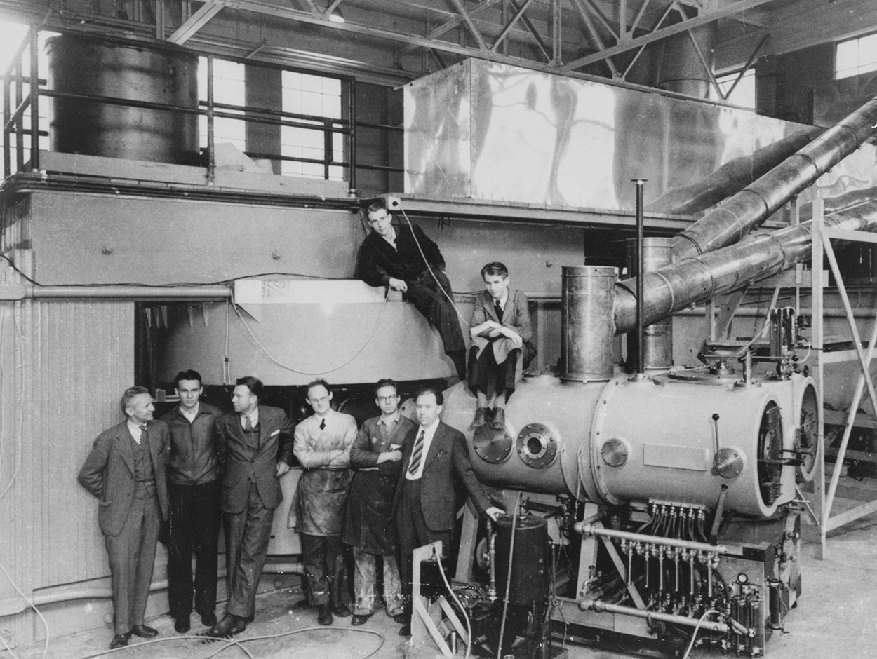 ไซโคลตรอนขนาด 1.5 m (60 in) หลังจากสร้างเสร็จในปี ค.ศ. 1939 บุคคลสำคัญในการพัฒนาและใช้งานแสดงอยู่จากซ้ายไปขวา: โดนัลด์ คุกซีย์, เดล อาร์. คอร์สัน, เออร์เนสต์ ลอว์เรนซ์, โรเบิร์ต แอล. ทอร์นตัน, จอห์น แบ็กคัส และวินฟิลด์ ซอลส์บิวรี ในพื้นหลังคือ ลูอิส วอลเตอร์ อัลวาเรซ และเอ็ดวิน แมคมิลแลน
