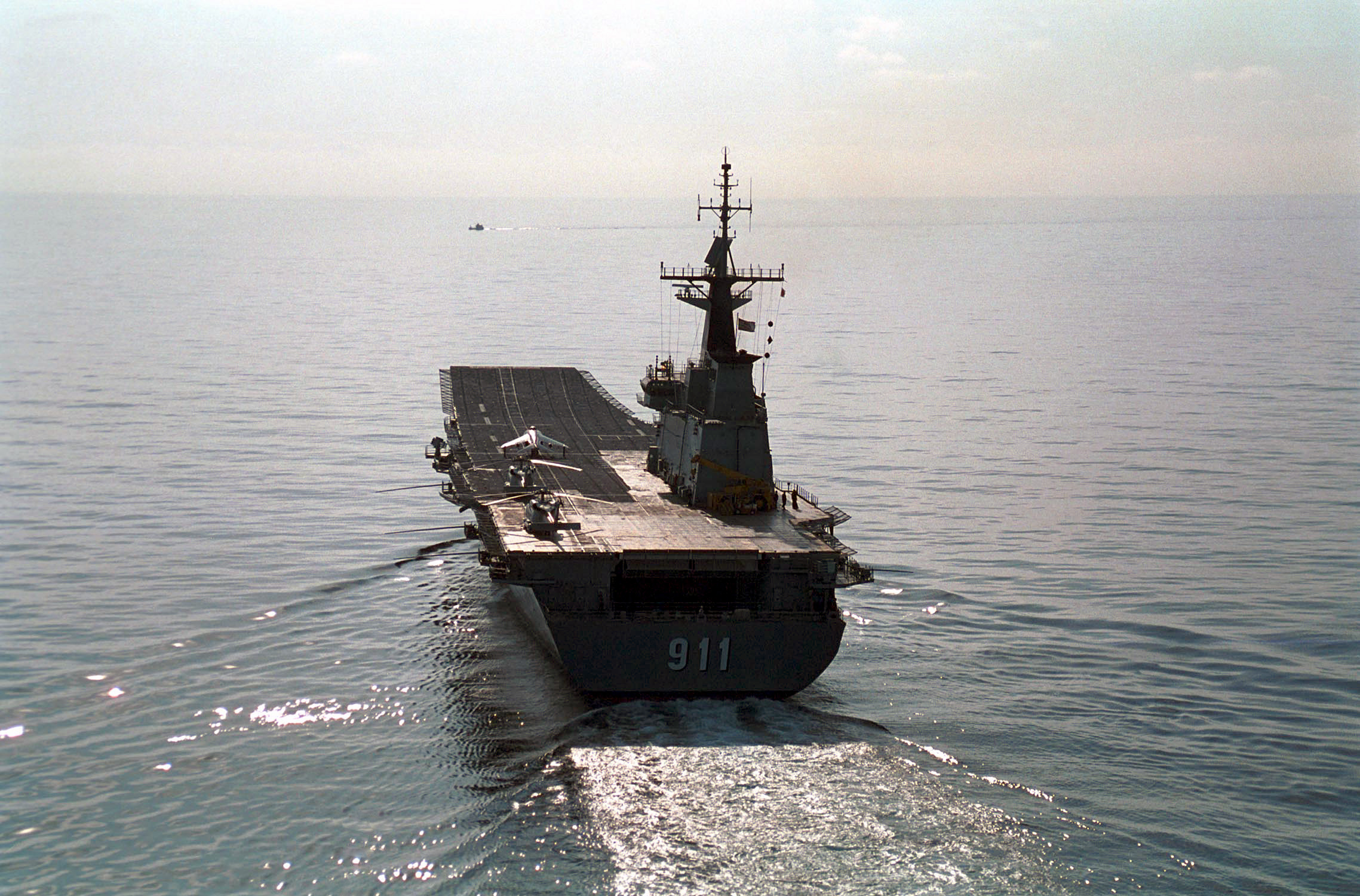 A small aircraft carrier photographed from behind as she sails across calm waters
