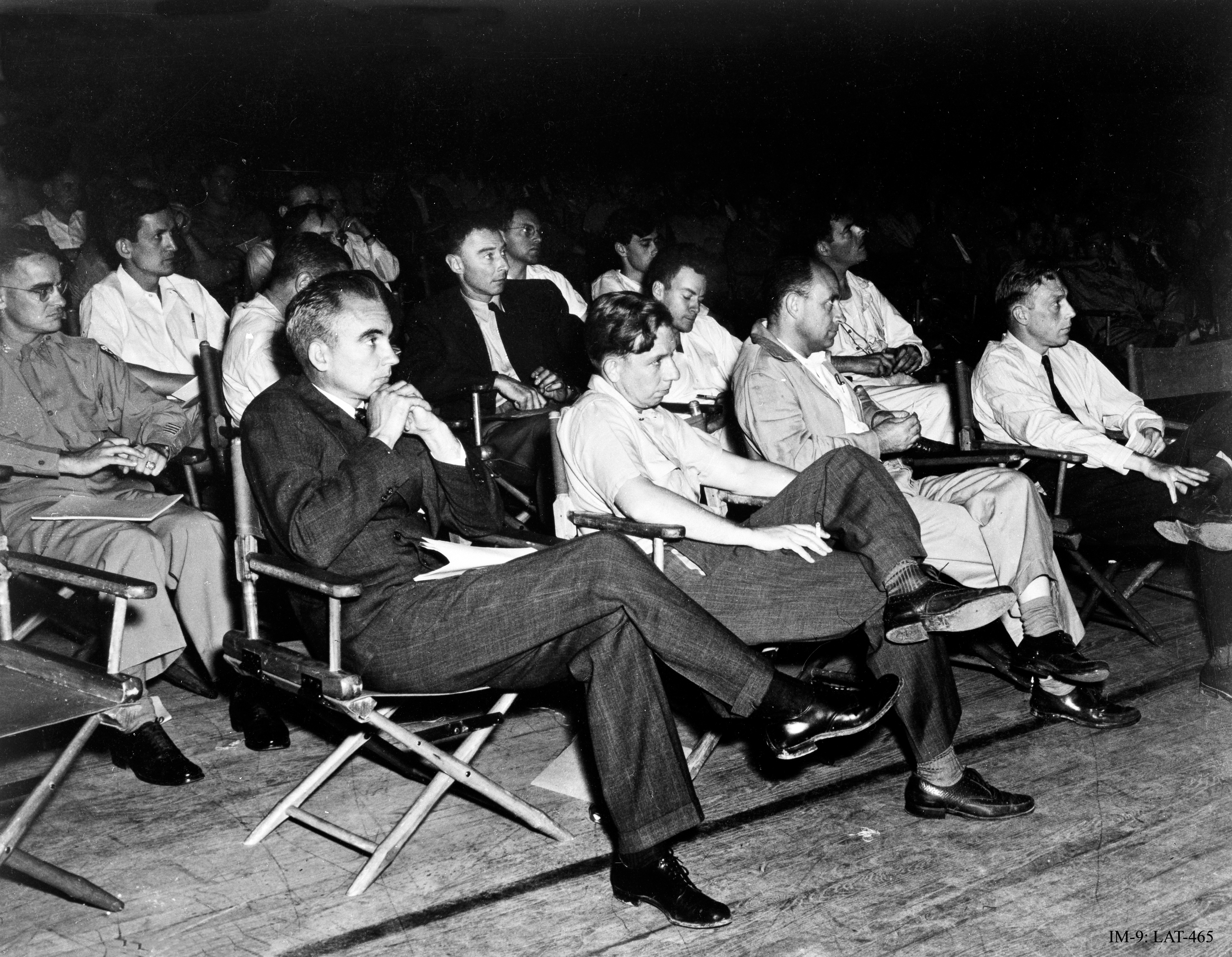 1946年のロスアラモス国立研究所における「スーパー」に関するコロキウム。前列にはノリス・ブラッドベリ、ジョン・H・マンリー、エンリコ・フェルミ、J.M.B.ケロッグが並ぶ。マンリーの後ろにはオッペンハイマー(ジャケットとネクタイ着用)がおり、その左にはリチャード・ファインマンがいる。一番左の陸軍大佐はオリバー・ヘイウッド。ヘイウッドとオッペンハイマーの間の3列目にはエドワード・テラーがいる。