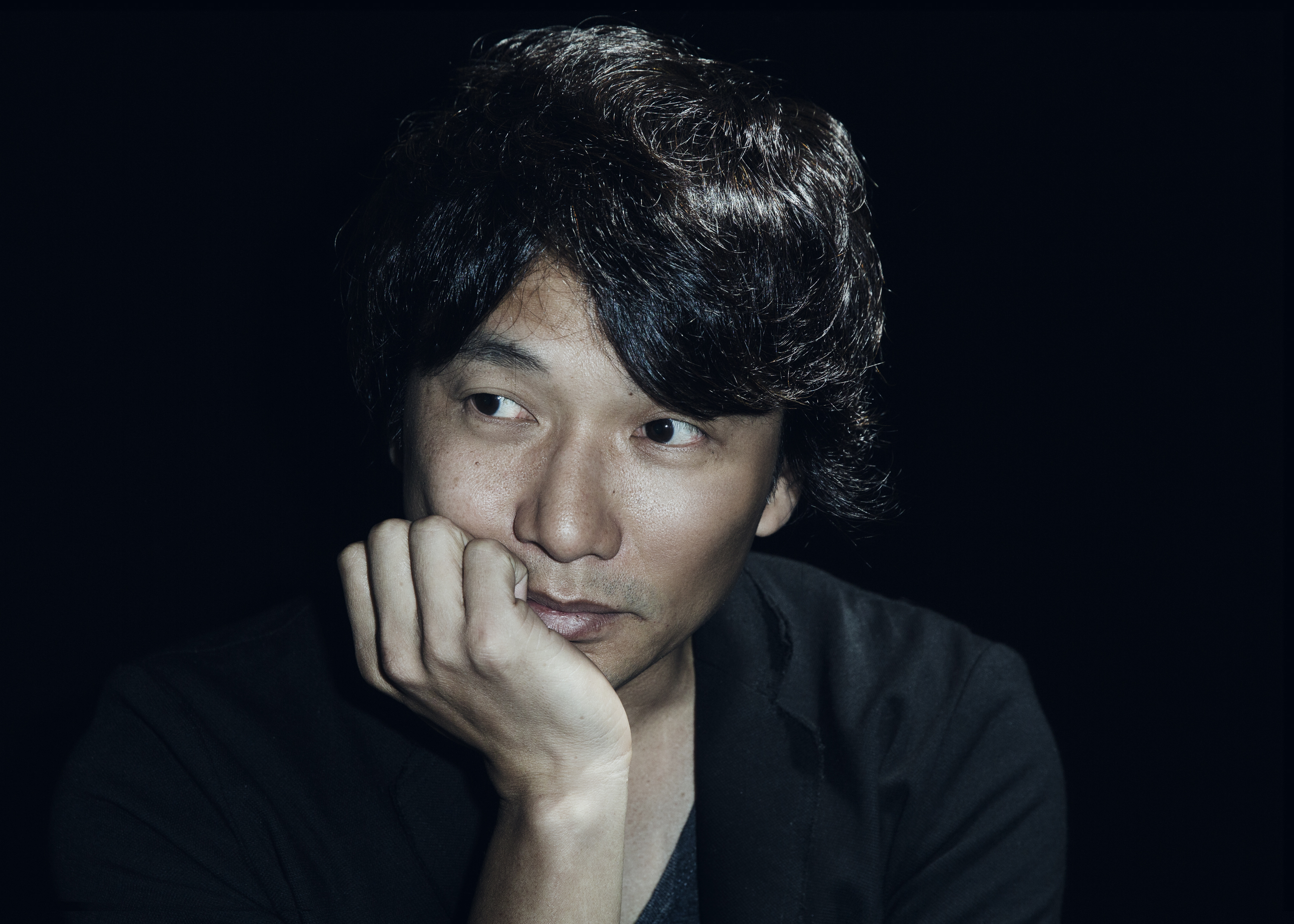 검은 셔츠를 입은 일본 남자가 오른쪽을 보며 생각하고 있다.