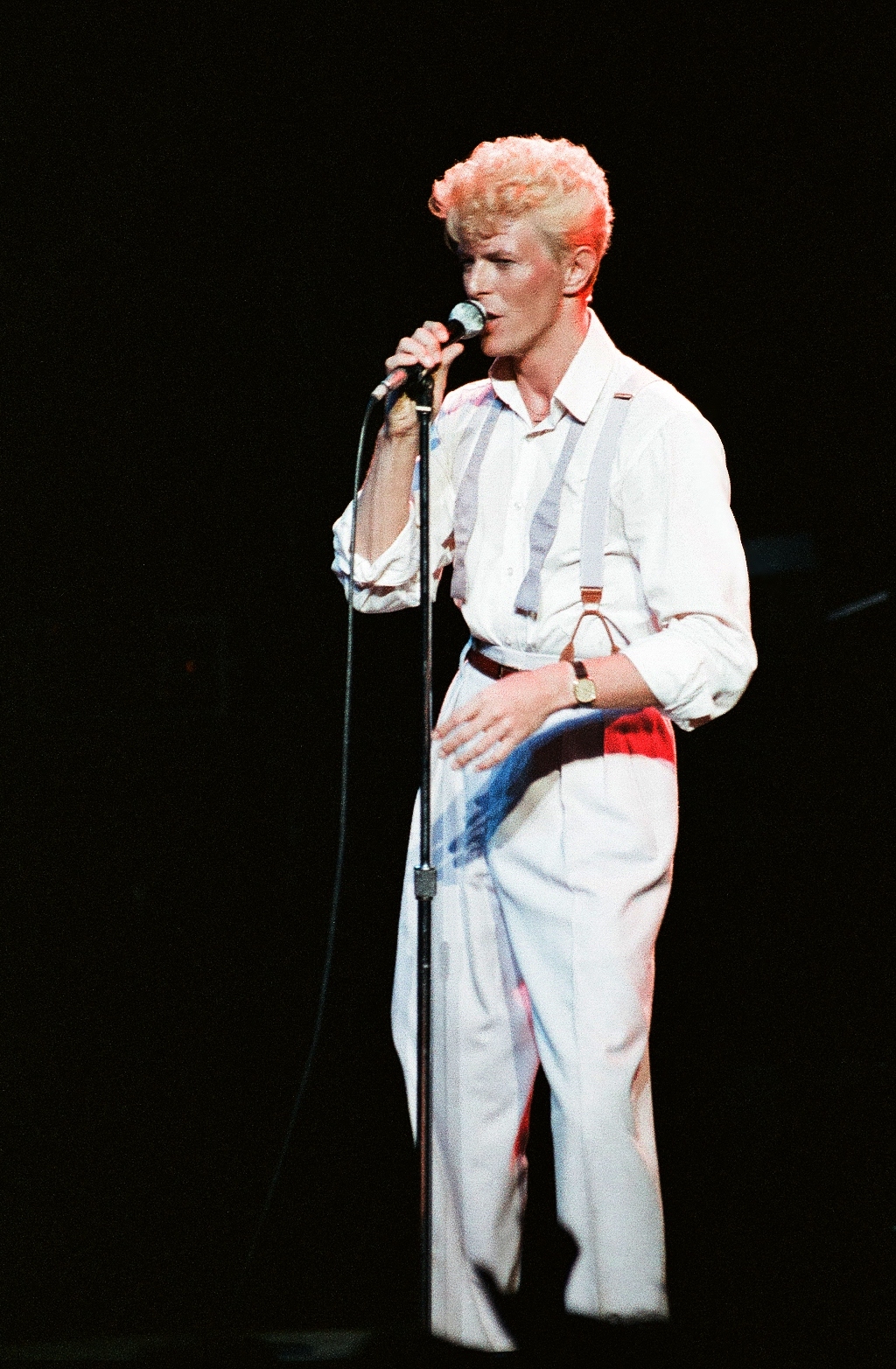 A man with blonde hair and a white suit holding a microphone
