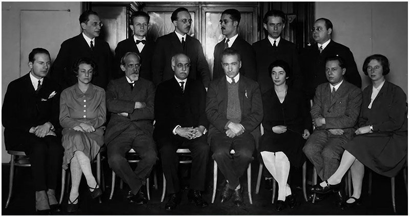 monochrome photograph of eight seated people, with a row of six people standing behind them