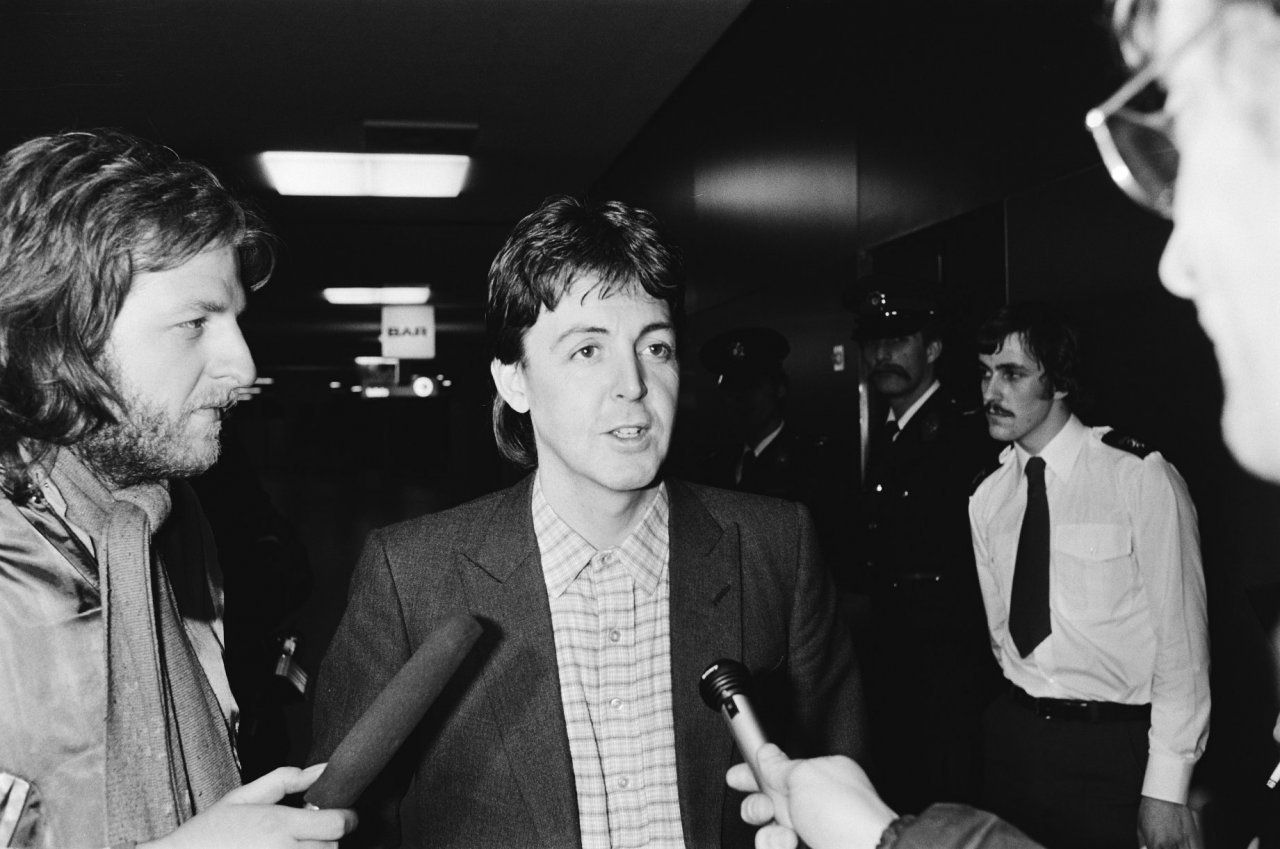 Paul McCartney being interviewed by two reporters holding microphones.