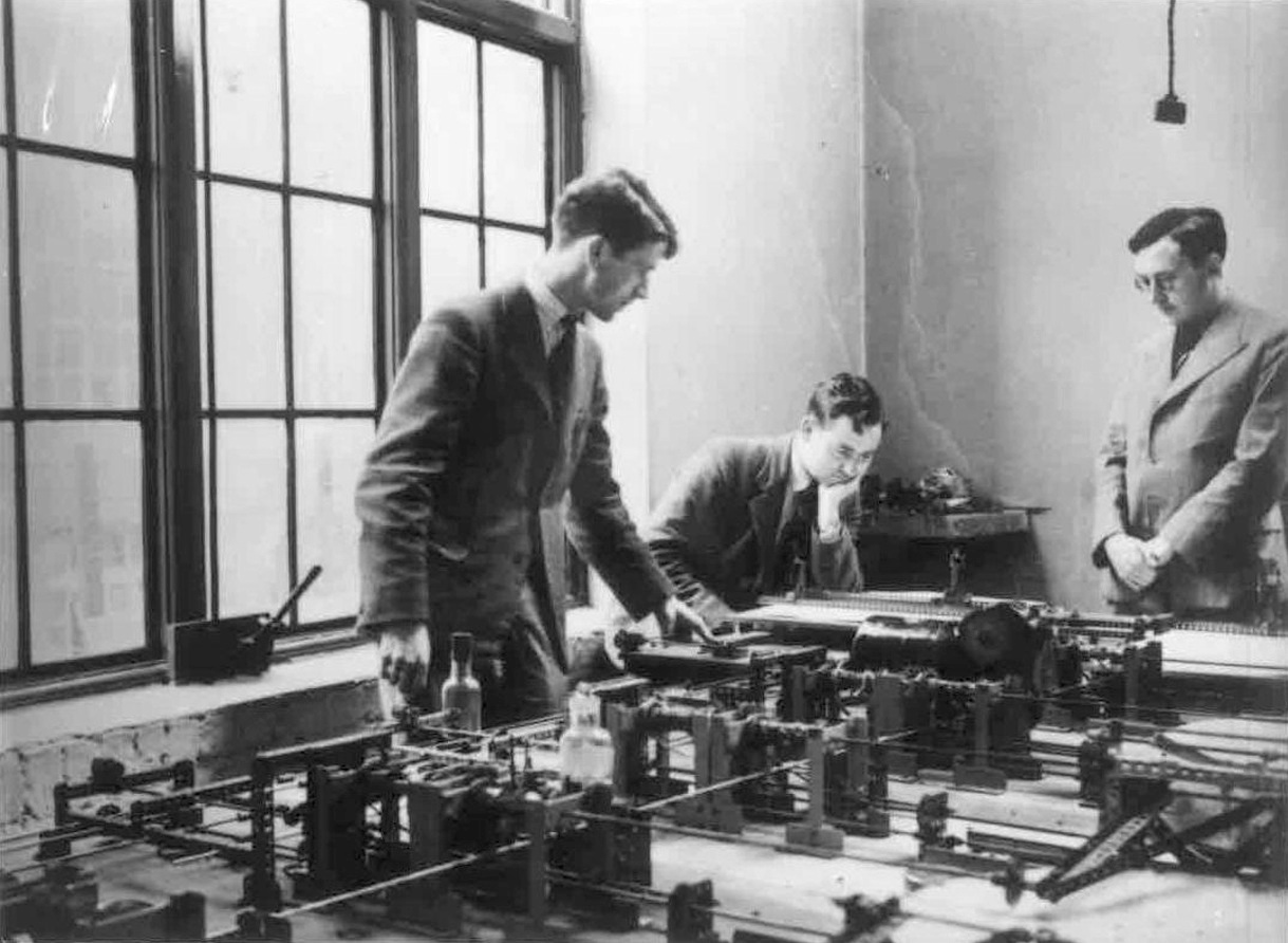 1937년 케임브리지 대학교 수학 연구소에서 메카노 미분 해석기 옆의 모리스 윌크스(오른쪽).