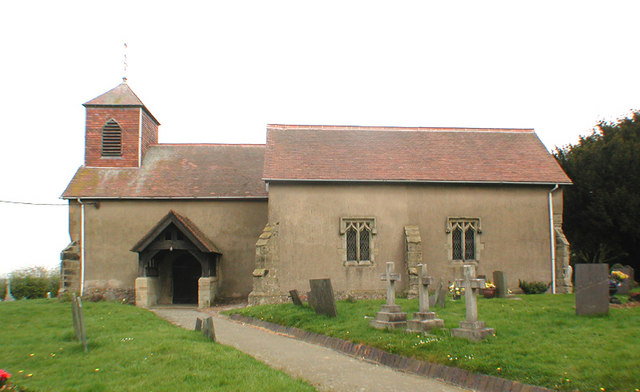 Side view of a building, which has a small tower on the left side: tombstones lie in rows on plots in front.