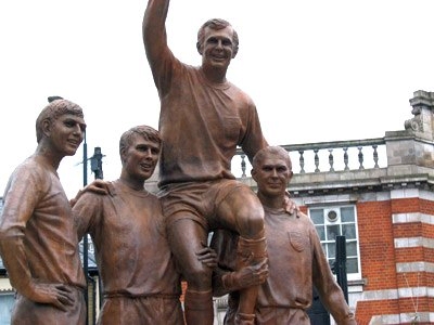 Patung Piala Dunia (The Champions) yang menampilkan Moore dengan trofi Piala Dunia, di bahu Geoff Hurst dan Ray Wilson, bersama Martin Peters (Lokasi: Jalan Barking di simpang Jalan Green, London E6).