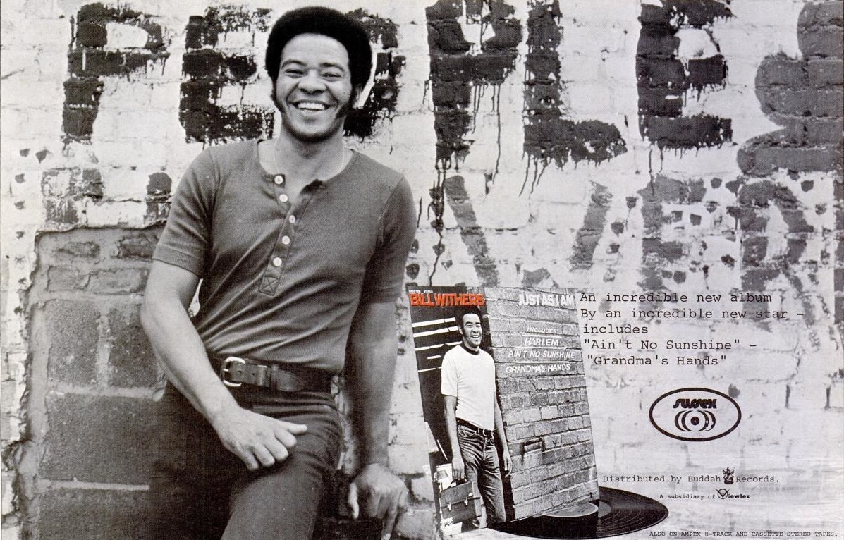 Withers smiling and leaning in front of a brick wall
