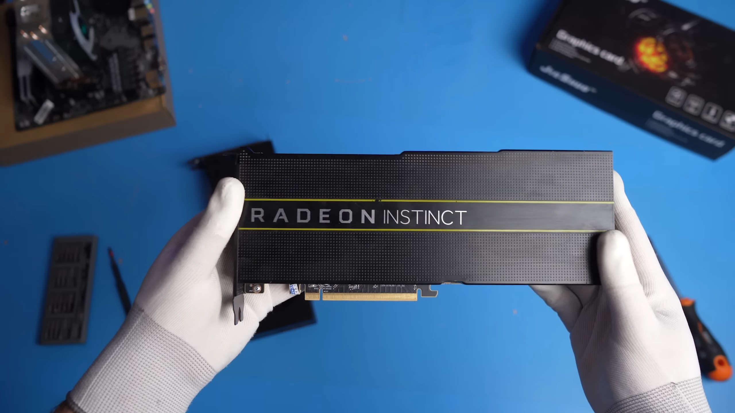두 개의 장갑을 낀 손이 AMD 라데온 인스팅트 MI50 카드를 들고 있다. 배경은 흐릿하다.