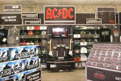 슈퍼마켓 내부, 비디오 게임 록 밴드 상자, 음악 CD 디스플레이, AC/DC 로고가 위에 있는 디스플레이로, 셔츠, CD, 록 밴드 악기가 특징입니다.
