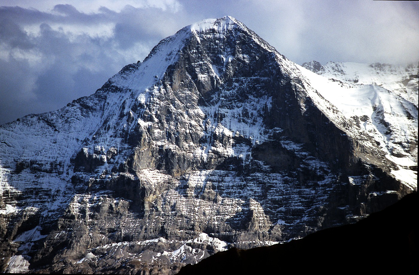 With sunlit snowfields and dark clouds in the distance