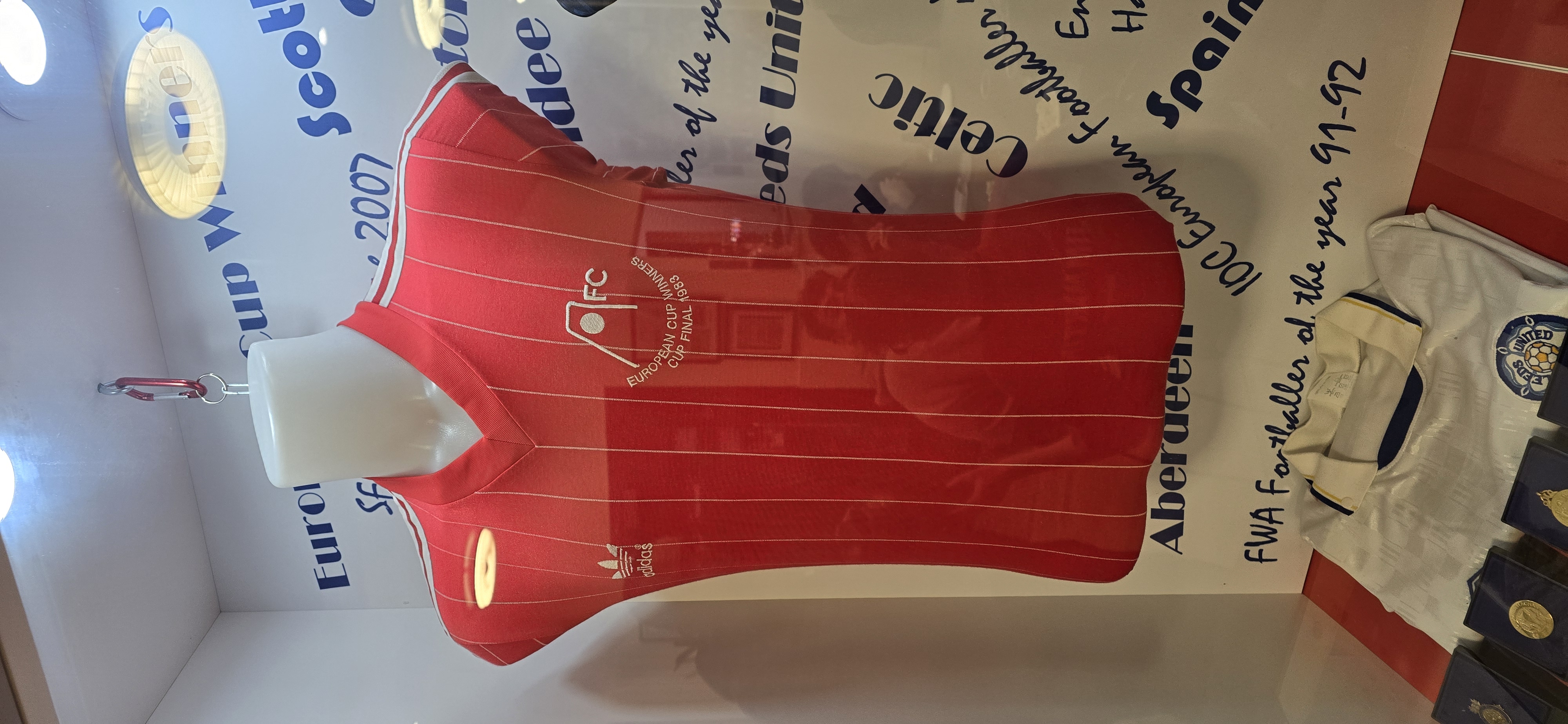 a red football shirt showing the Aberdeen FC insignia and text showing it is from the European Cup Winners Cup final 1983