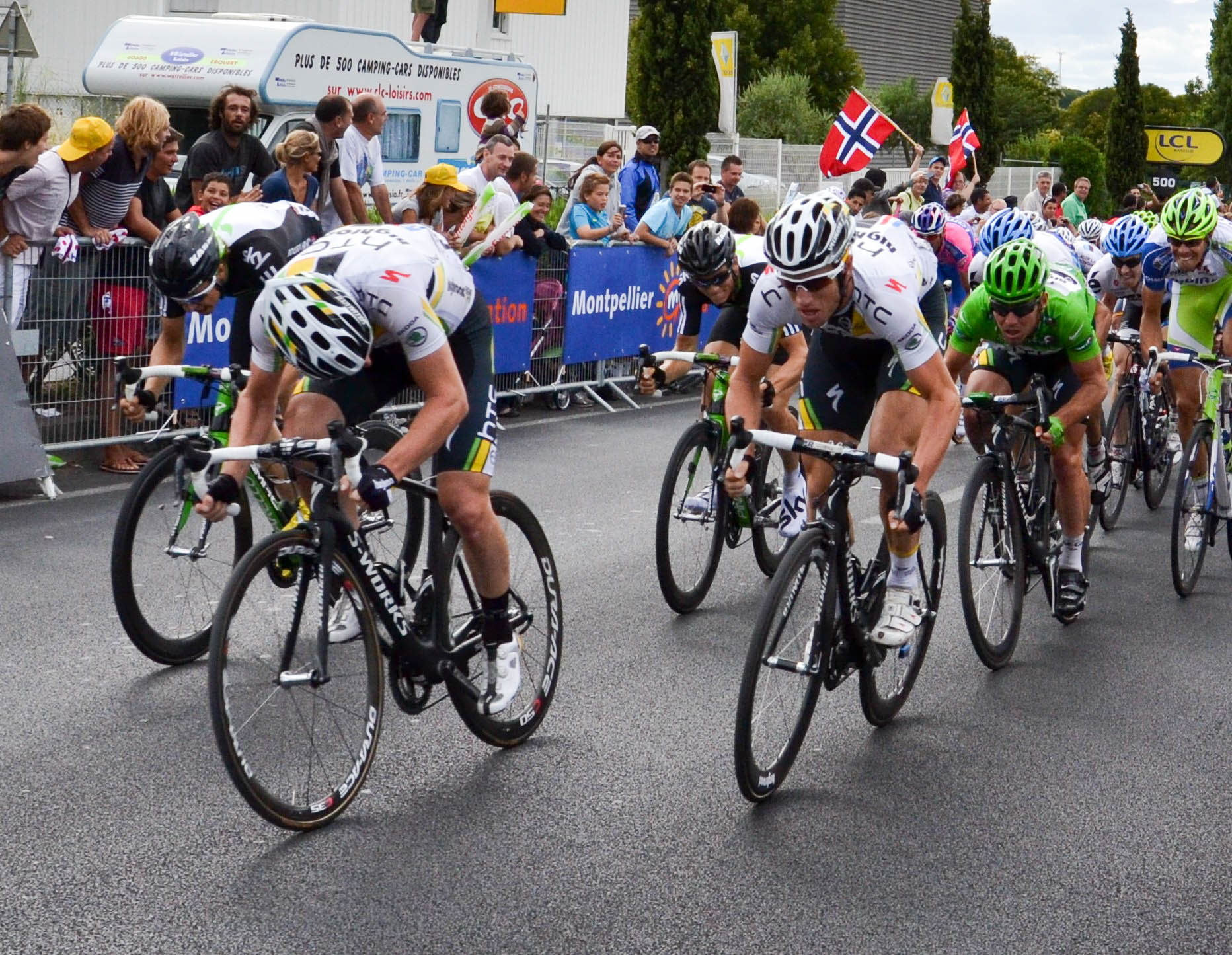 A number of cyclists are pictured sprinting along a road with a crowd watching them 