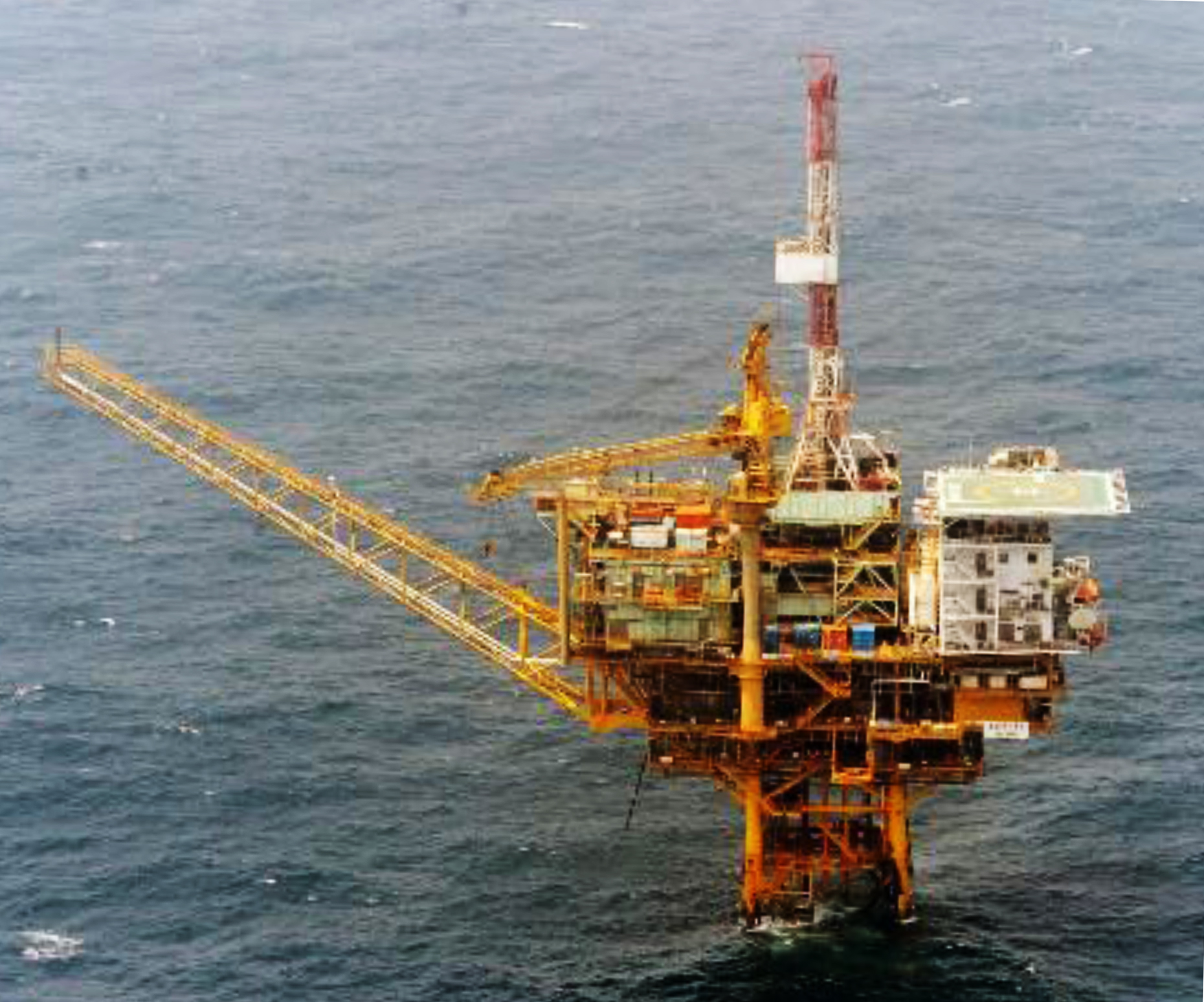 A yellow oil rig in the ocean pointing left