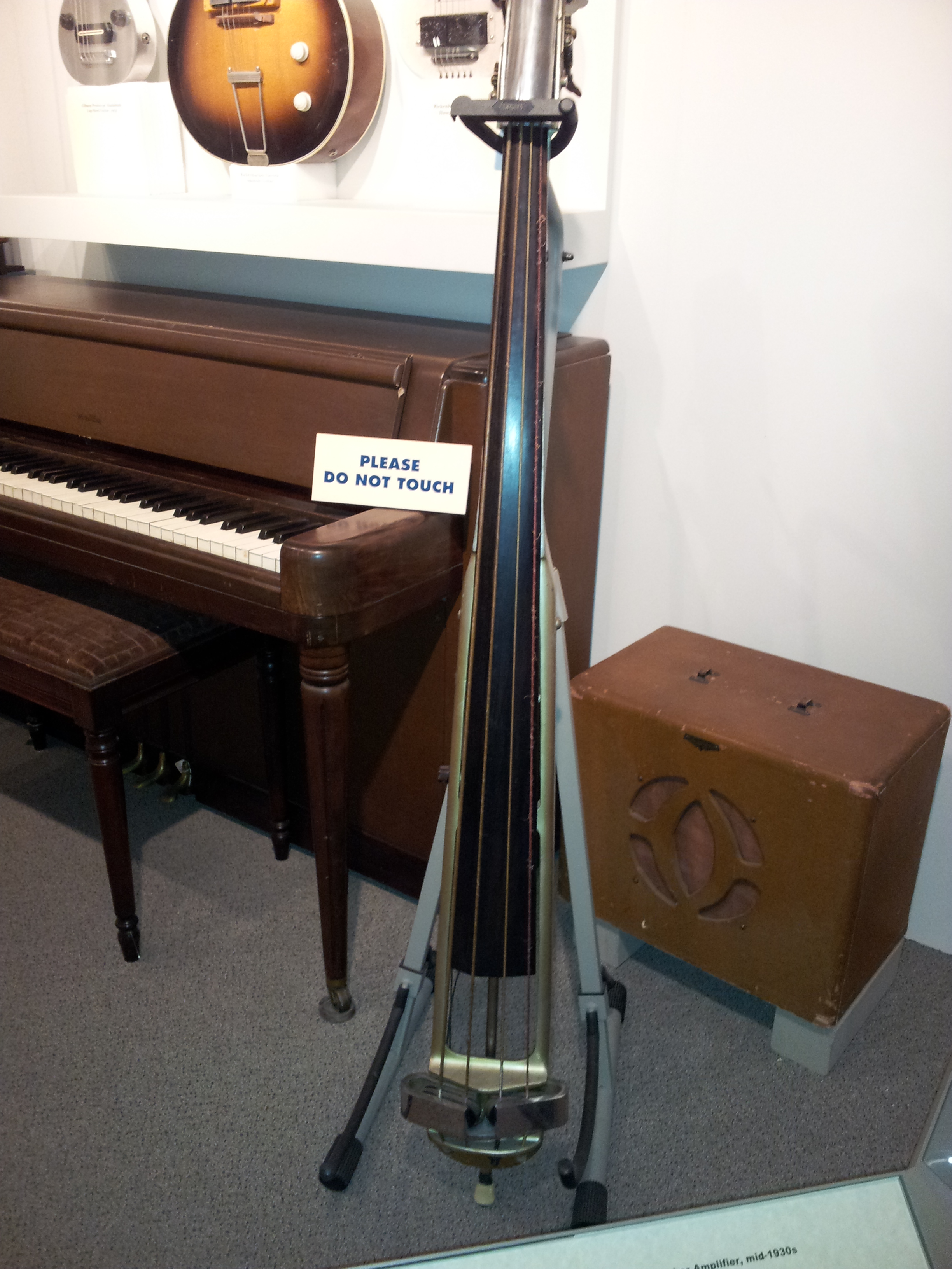 A museum exhibit of vintage musical instruments shows a 1930s amplifier and speaker cabinet and an upright bass with a pickup.