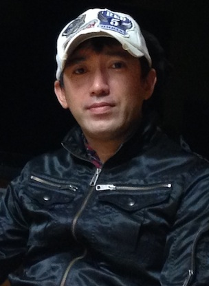 A photograph of a Japanese man wearing a baseball cap.