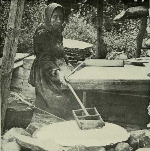A Norwegian peasant woman baking flatbread in a traditional manner, circa 1910s.