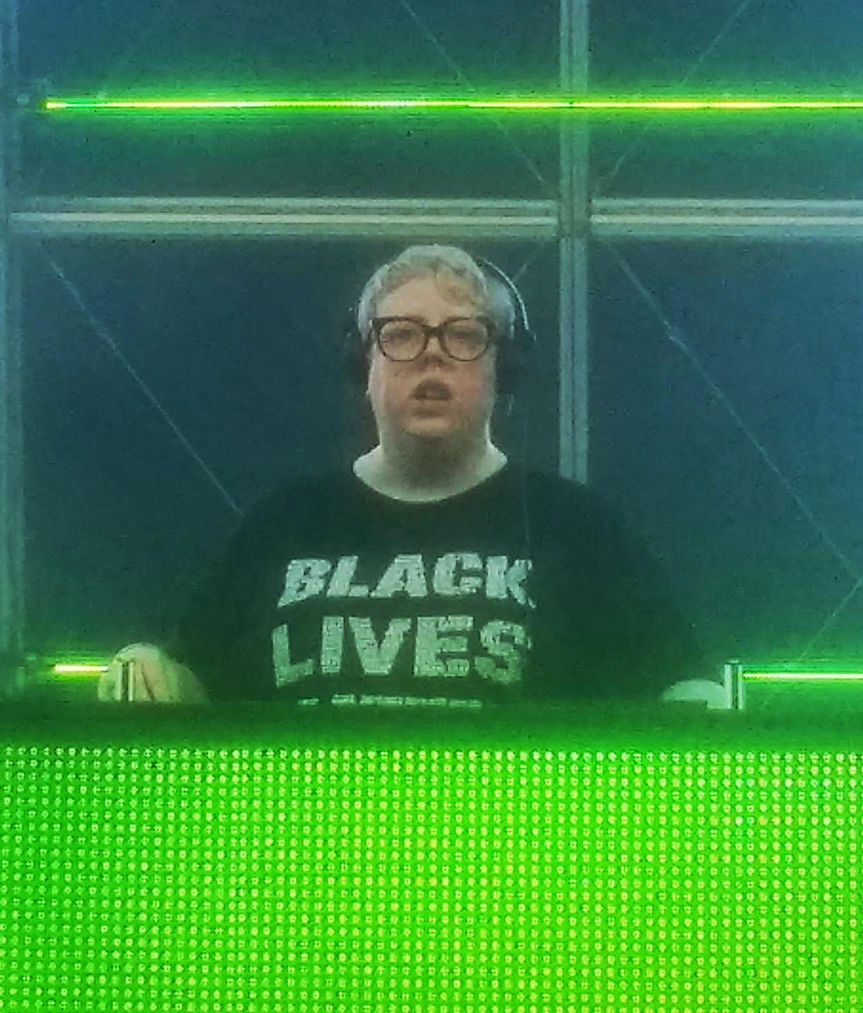 The Blessed Madonna performing on a green-lit stage wearing a black shirt that says 