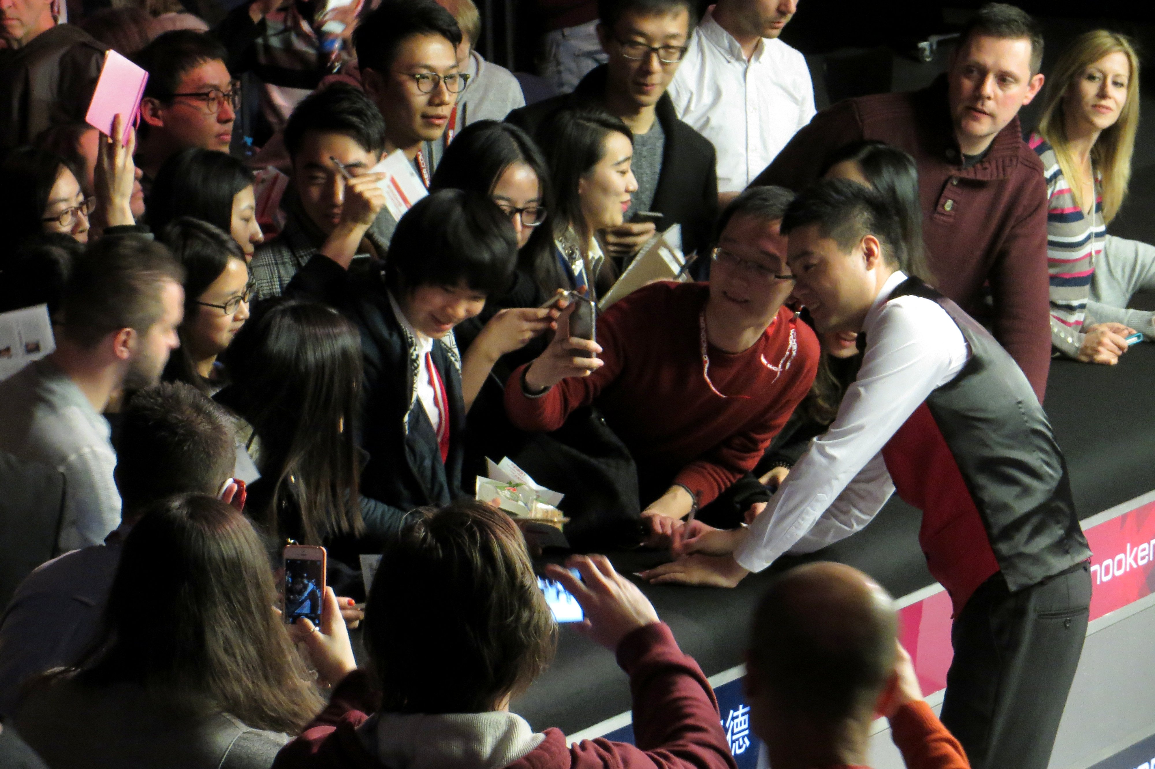 Ding poses for a photograph with a fan. Many other fans are nearby.