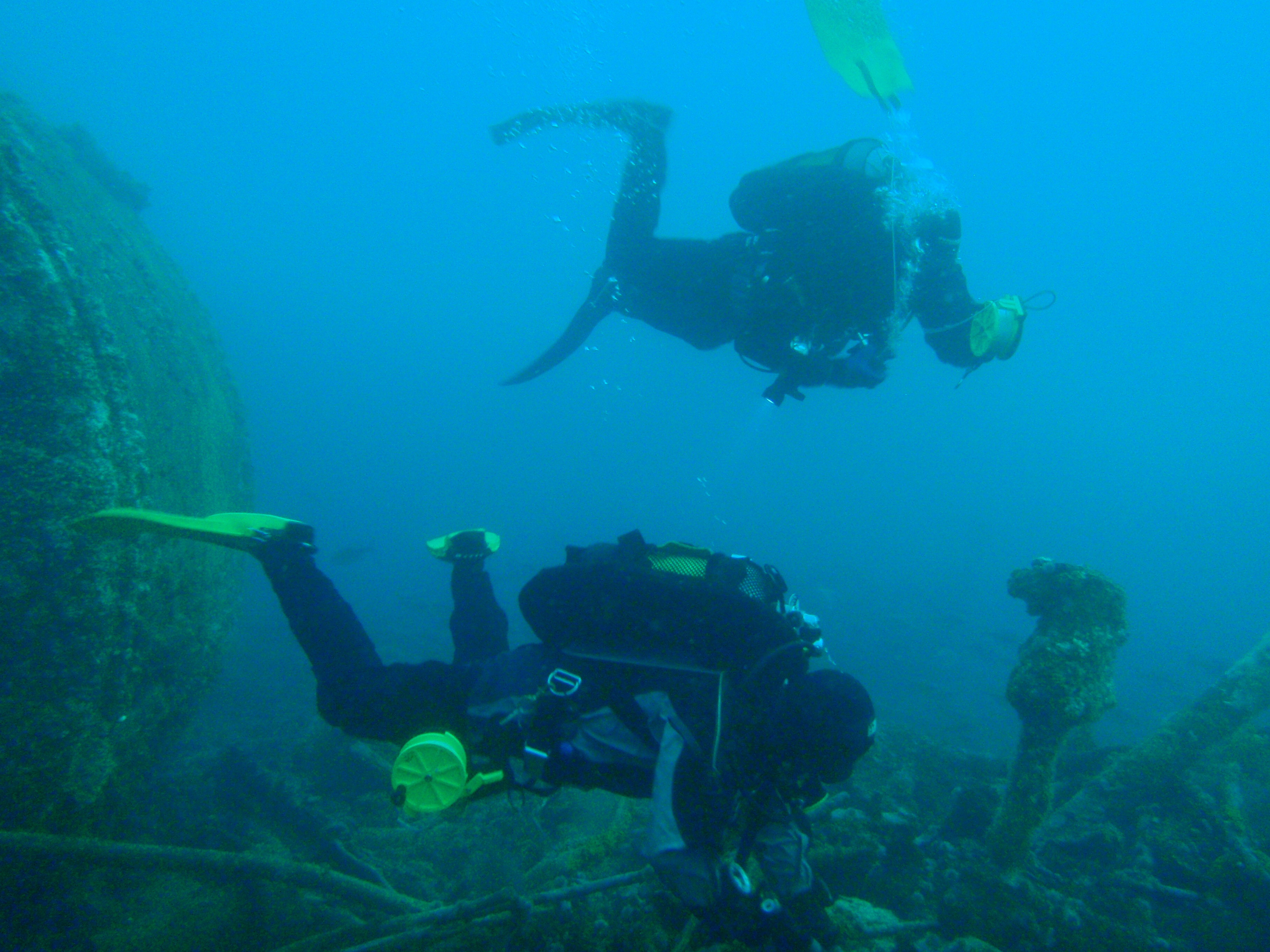 Two divers on a wreck. The one in the background is deploying an inflatable surface marker buoy as preparation for ascent
