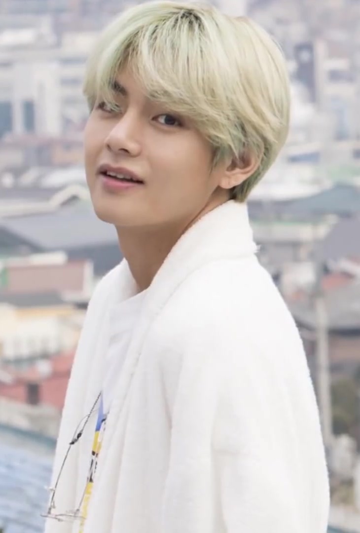V, in all white, smiles and faces left
