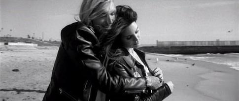 해변가에서 서로에게 매달려 서 있는 갈색 머리의 여성과 긴 머리 남자의 흑백 초상화.