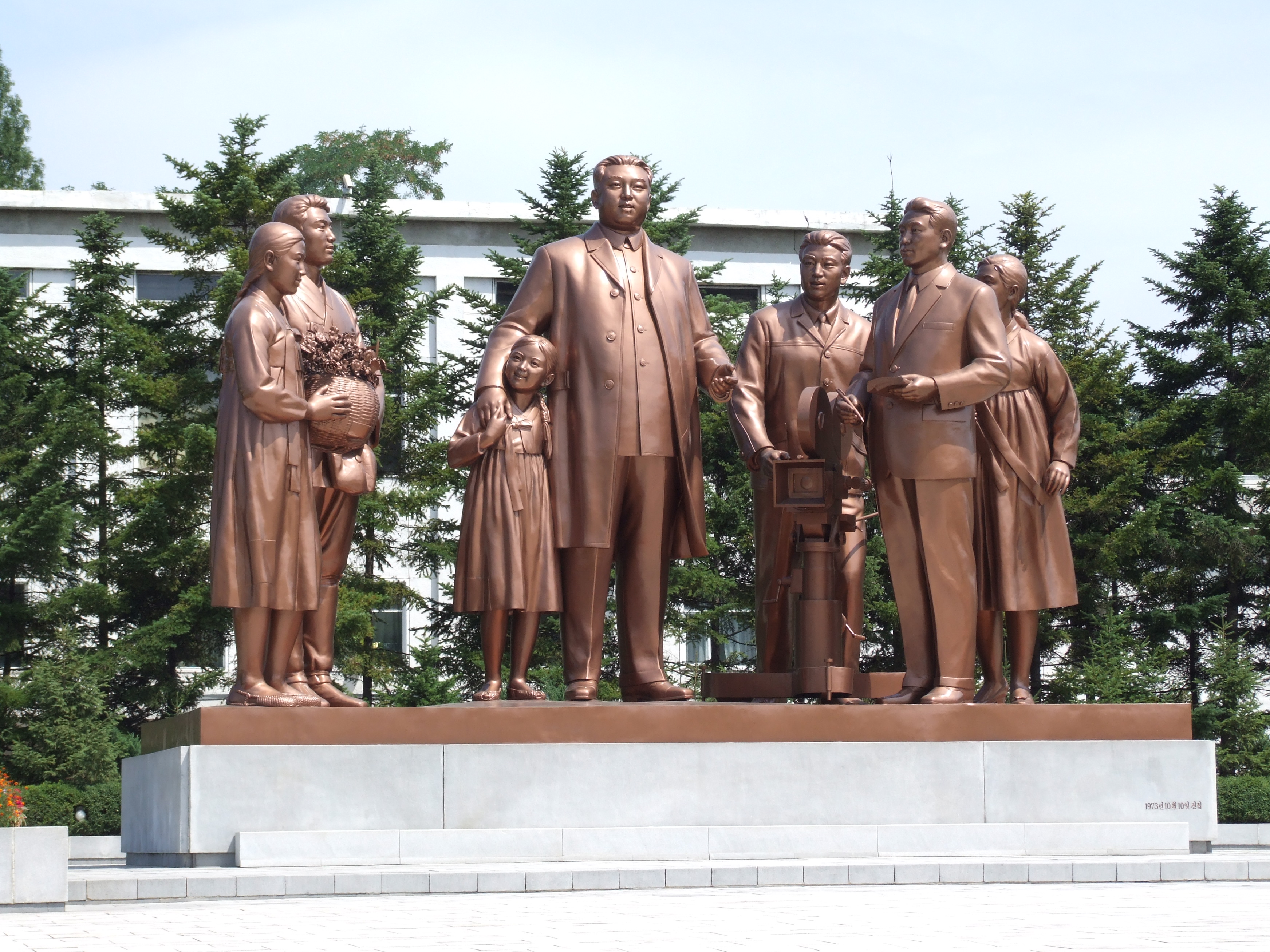 김일성 동상과 카메라, 꽃바구니, 공책을 든 여섯 명의 조각상