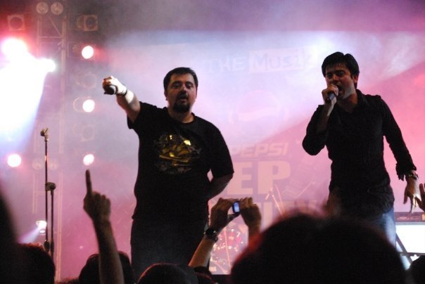 Khan and Ahmed Ali Butt onstage; Khan is singing, and Butt is holding his microphone to the audience