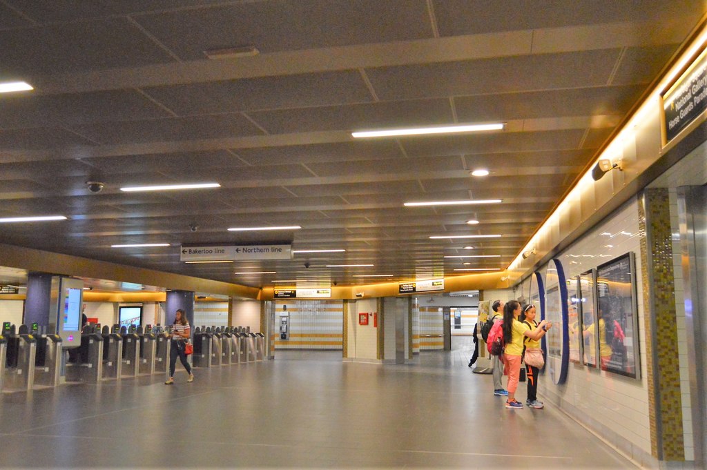 타일 바닥과 가끔 조명이 켜진 매달린 천장이 있는 넓고 밝은 공간. 왼쪽에 개찰구가 줄지어 있다