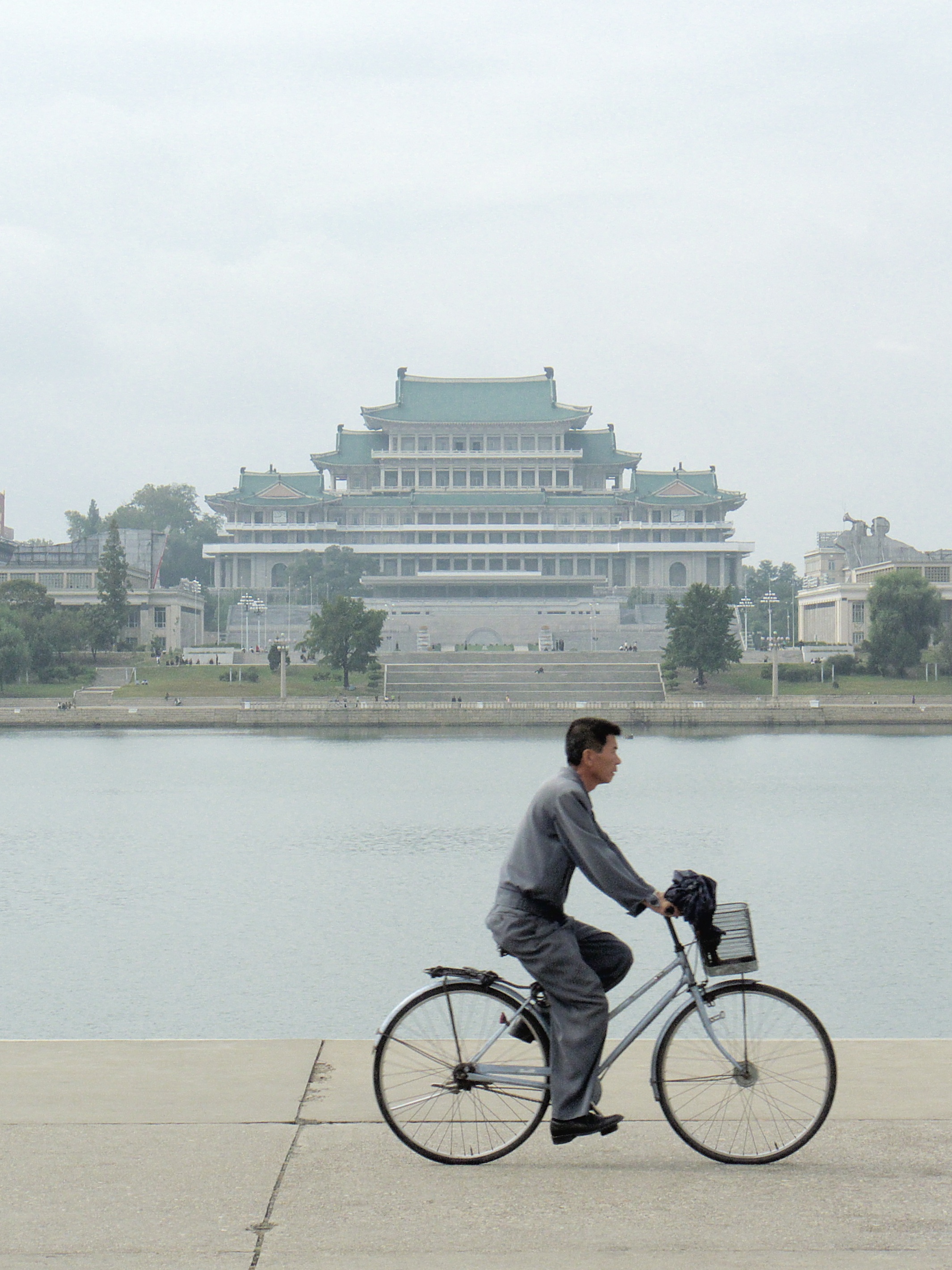 A uniformed civilian man riding a bicycle in Pyongyang. Such uniforms are part of nationally mandated dress codes.