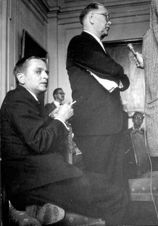 1964年、記者からの質問に答えるエルランデル(右、立っている)とオロフ・パルメ(左、座っている)。