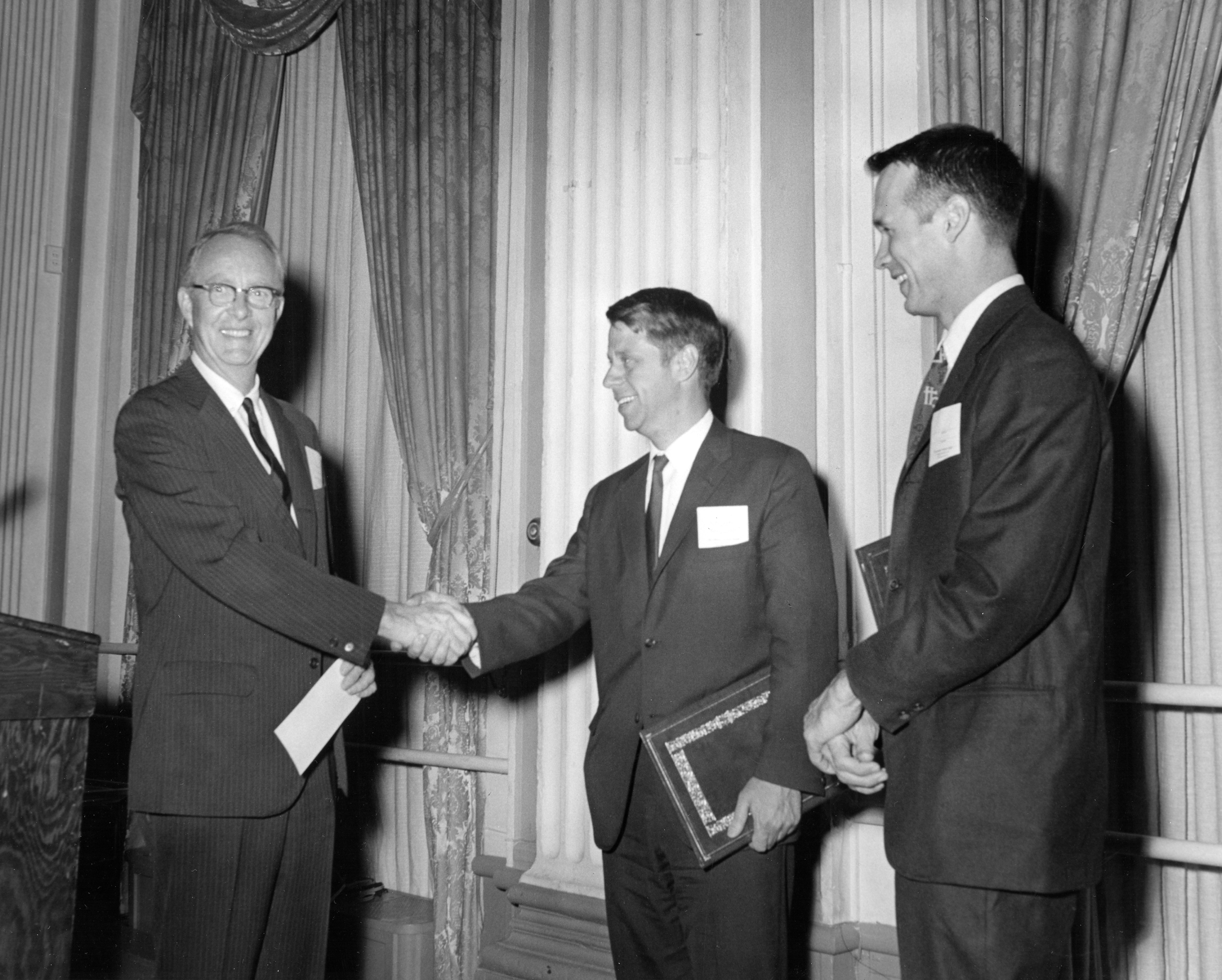 1969년 올리버 E. 버클리 응집 물질 물리학상 시상식. 루이스 월터 알바레즈(왼쪽)가 데이비드 길버트 토마스(중앙)와 존 홉필드(오른쪽)를 축하하고 있다.