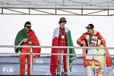 Antonelli wearing his gold medal on the podium of the 2022 FIA Motorsport Games alongside Manuel Espírito Santo and Bruno del Pino, with the Italian flag draped over him.